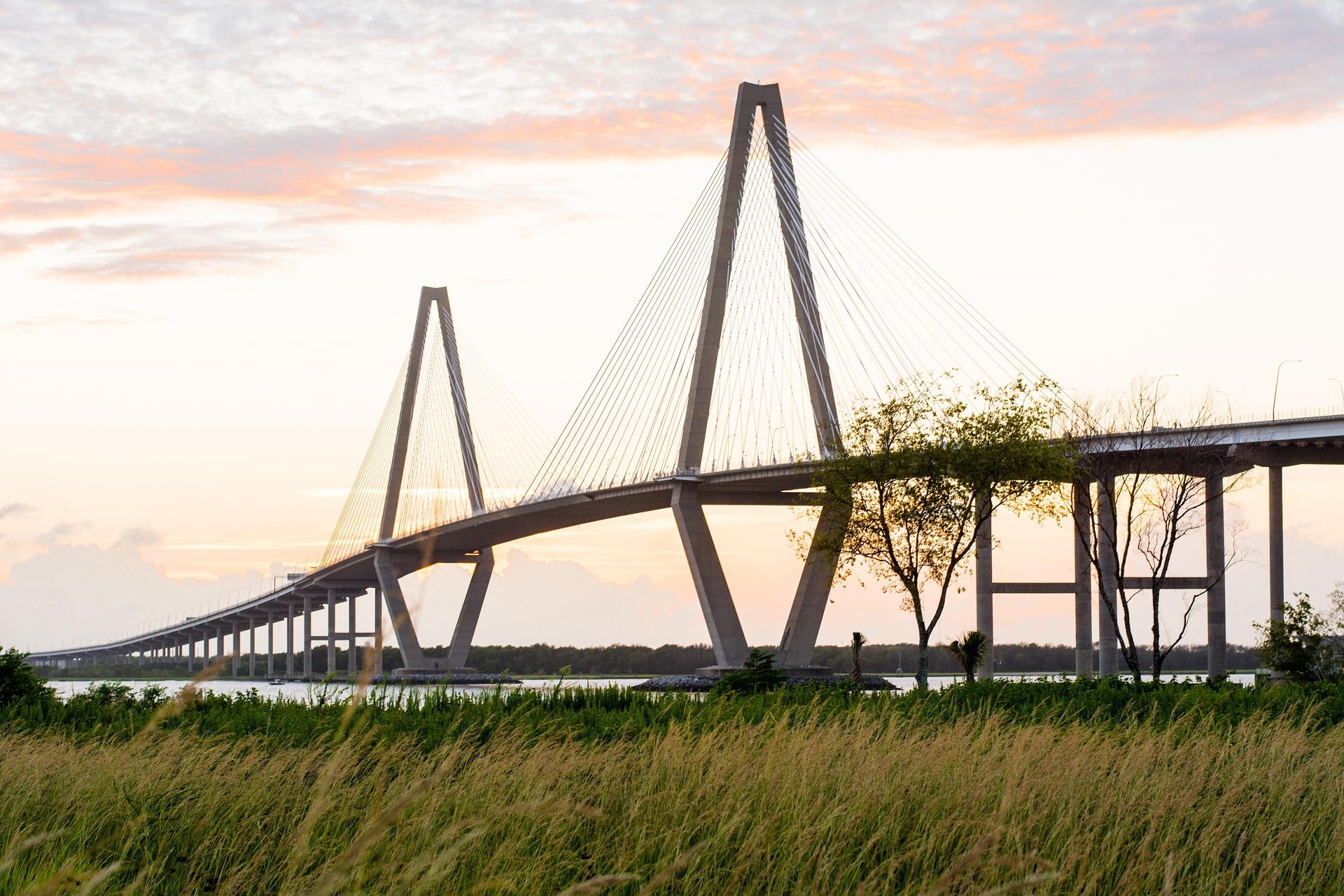 Arthur Ravenel Jr. Bridge spanning the Cooper River in Charleston, South Carolina at sunset, showing its two diamond-shaped cable-stayed towers against a colorful sky with marsh grass in the foreground.